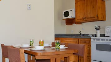A dining area with wooden chairs and a table set for four, a microwave, and a stove in the kitchen area.