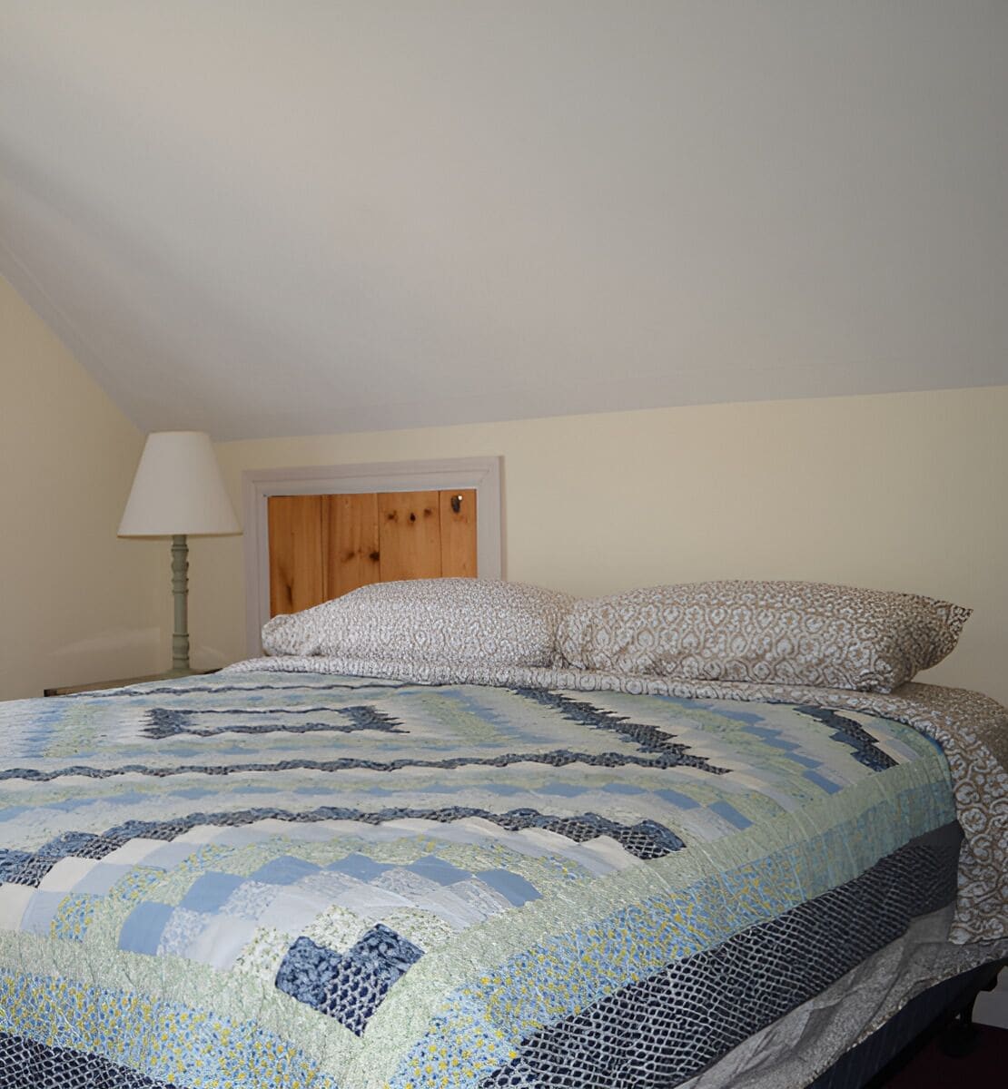 A bedroom with a bed, a wooden headboard, a nightstand, and a lamp.