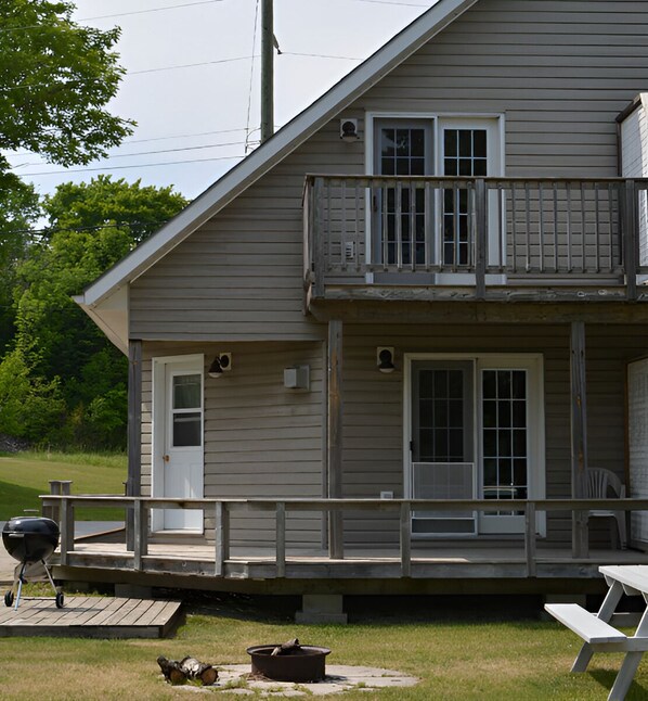 Une maison à deux étages dotée d’un balcon, d’une porte d’entrée et d’une terrasse avec un barbecue et une table de pique-nique.