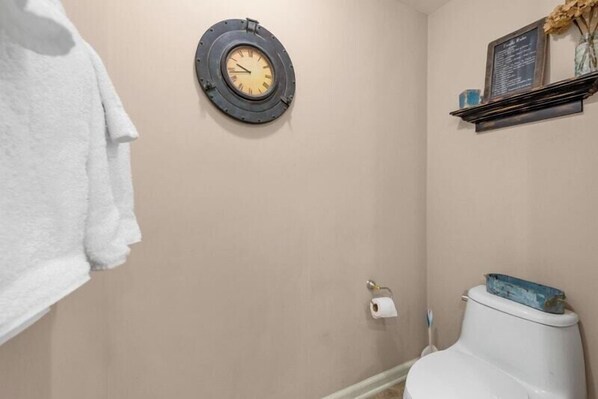 A bathroom with a round clock, a toilet, and a shelf with a chalkboard. - Spacious Oceanview Three Bedroom Luxury Condo | Margate Towers 2008 (Myrtle Beach)