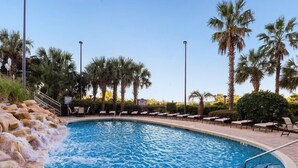 A pool with a waterfall feature, surrounded by lounge chairs and palm trees.