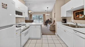 A modern kitchen with white cabinetry, a built-in oven, and a dining area with a table and chairs. - Golf Villa Charm | Poolside Views | Relax in Style |  Magnolia North 4847-303 (Myrtle Beach)