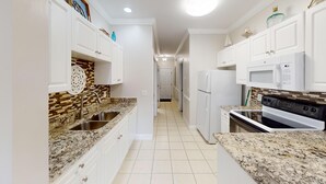 A kitchen with white cabinets, a granite countertop, a stainless steel sink, a white refrigerator, a microwave, and a stove. - Cozy Golf Villa | Pool View Paradise | Relax | Magnolia North 4872-203 (Myrtle Beach)