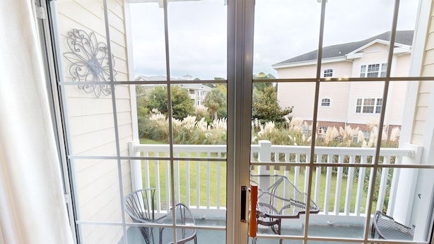 A balcony with a white railing, two metal chairs, and a metal table. - Cozy Golf Villa | Pool View Paradise | Relax | Magnolia North 4872-203 (Myrtle Beach)