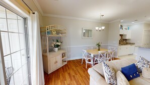 A dining area with a wooden table and white chairs, a white sofa with patterned cushions, and a wooden cabinet with a mirror above it. - Cozy Golf Villa | Pool View Paradise | Relax | Magnolia North 4872-203 (Myrtle Beach)
