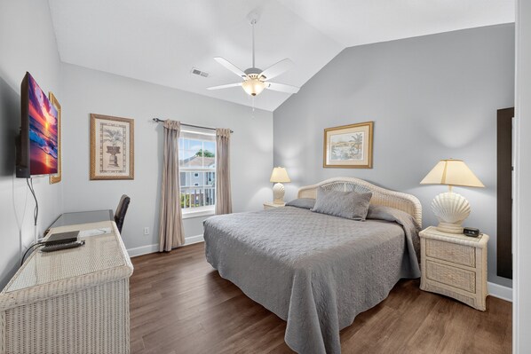 A bedroom with a bed, a desk, a chair, a ceiling fan, and two bedside tables with lamps.