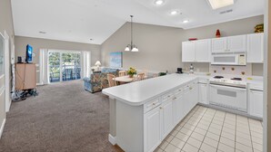 A modern kitchen with white cabinetry, a large island, and a dining area with a sofa and chairs. - MN 4811-304 | Stay in Golf Paradise Book for Golf Season (Myrtle Beach)