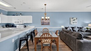 A modern kitchen with white cabinets, a microwave, and a dining area with a glass table and wicker chairs. - Pool View Bliss | Relax & Unwind | Myrtle Beach Awaits | Magnolia North 4827-202 (Myrtle Beach)