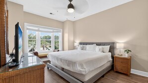 A bedroom with a large bed, a television on a glass table, and a nightstand with a lamp. - Pool View Bliss | Relax & Unwind | Myrtle Beach Awaits | Magnolia North 4827-202 (Myrtle Beach)