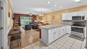 A modern kitchen with white cabinets, a built-in island, stainless steel appliances, and a dining area with a sofa and table. - Poolside Bliss | Golf Course Views | Ultimate Getaway | Magnolia North 4851-104 (Myrtle Beach)