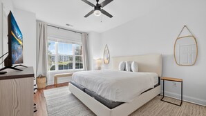 A modern bedroom with a large bed, a ceiling fan, a TV, and a window with curtains. - Refreshed Magnolia Pointe Condo Near the Coast | Magnolia Pointe Luster Leaf 4855-101 (Myrtle Beach)