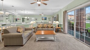 Ein geräumiges Wohnzimmer mit großem Fenster, Deckenventilator und Couchtisch aus Holz.