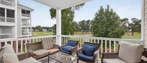 Eine überdachte Veranda mit Korbmöbeln und einem Glastisch, mit Blick auf einen Golfplatz.