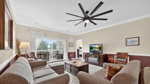 A living room with a ceiling fan, a television, and a view of the outdoors through large windows. - Spring Golf-View Rentals at Magnolia Pointe | Magnolia Pointe Luster Leaf 4878-201 (Myrtle Beach)
