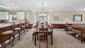 A spacious dining area with a large wooden table and chairs, a chandelier, and a view of the kitchen. - Spring Golf-View Rentals at Magnolia Pointe | Magnolia Pointe Luster Leaf 4878-201 (Myrtle Beach)