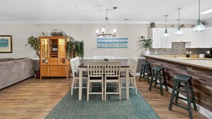 A modern kitchen with white cabinets, a wooden dining table, and bar stools. - Tranquil Garden Oasis | Pool & Golf Views | Magnolia Pointe Luster Leaf 4882-104 (Myrtle Beach)