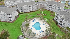 A residential complex with multiple two-story buildings, a central swimming pool, and surrounding green lawns. - Tranquil Garden Oasis | Pool & Golf Views | Magnolia Pointe Luster Leaf 4882-104 (Myrtle Beach)