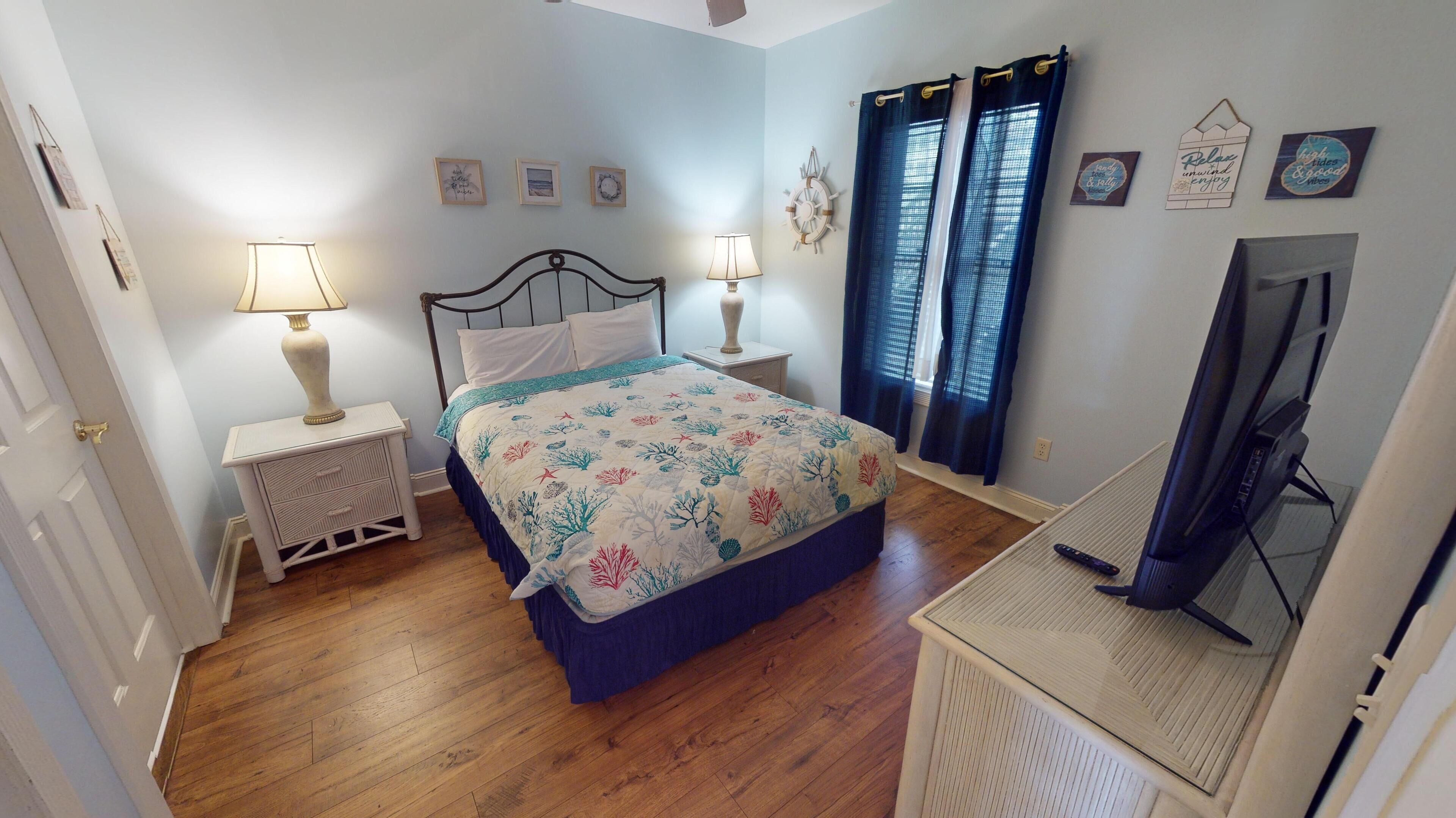 Quarto com cama, duas mesas de cabeceira com luminárias, televisão e uma parede decorada.