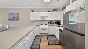 A modern kitchen with white cabinets, a stainless steel refrigerator, a microwave, and a gas stove.