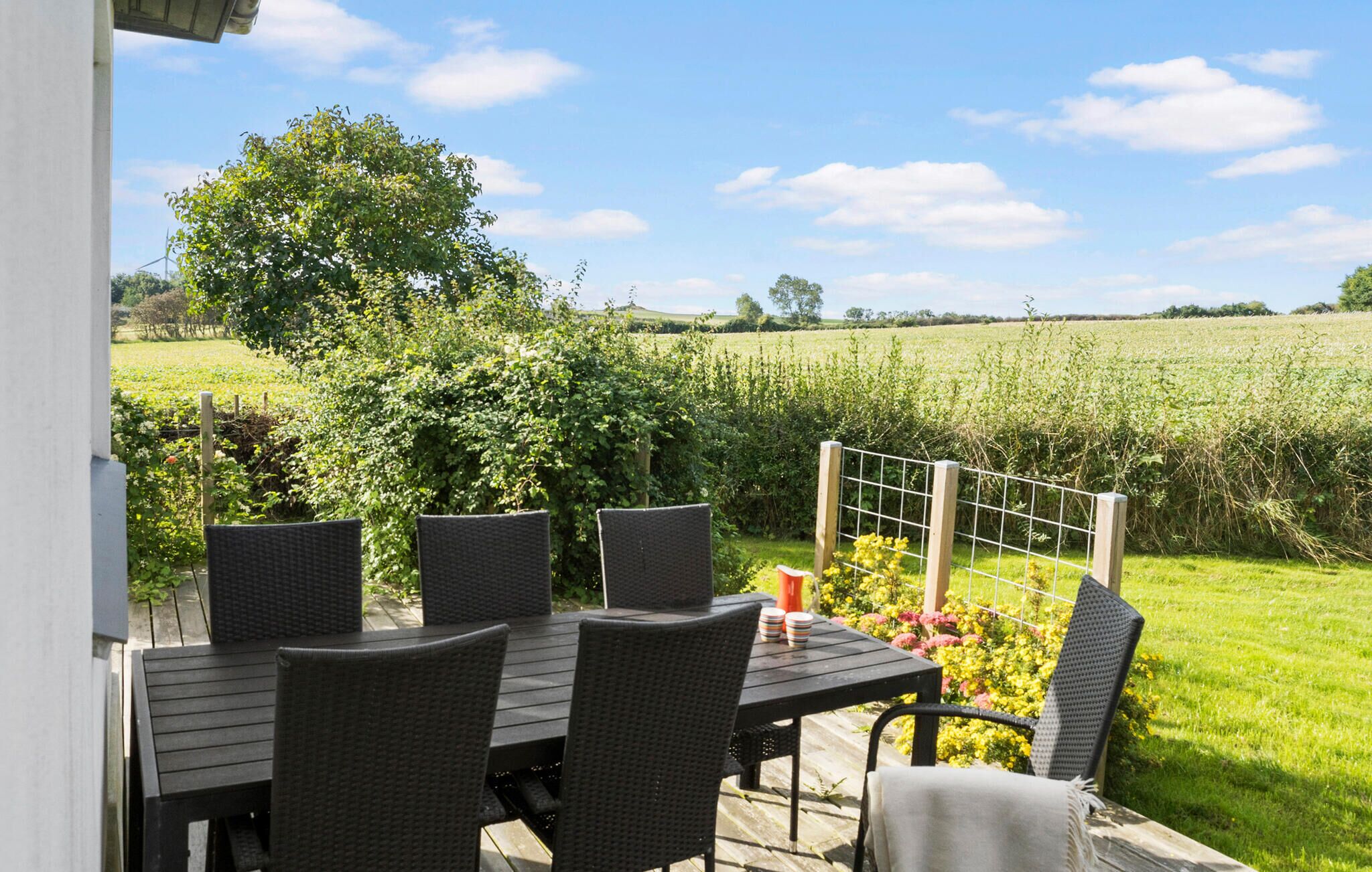 Eine Terrasse im Freien mit Tisch und Stühlen, umgeben von einem Garten und einem Feld.