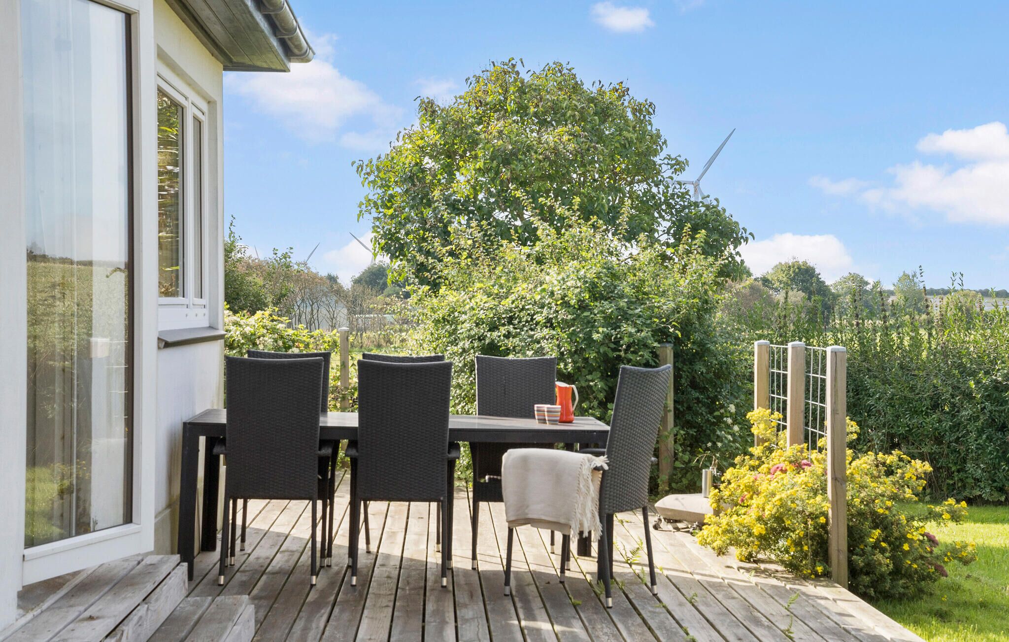 An outdoor patio with a table and chairs, a wooden deck, and a view of a tree and landscape.