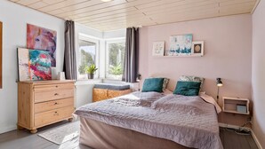A bedroom with a large bed, a wooden dresser, a window with curtains, and wall art.
