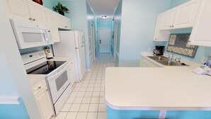 A kitchen with white cabinets, a microwave, an oven, a refrigerator, a sink, and a coffee maker.
