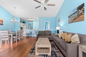 A living room with a gray sofa, wooden coffee table, and a dining area with chairs and a table. - Serene Garden Views | Beach & Golf Retreat | Magnolia Place 4627-302 (Myrtle Beach)