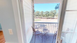 A balcony with two chairs and a small table, overlooking a golf course.