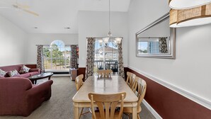 A dining area with a wooden table and chairs, a sofa, and a ceiling fan.