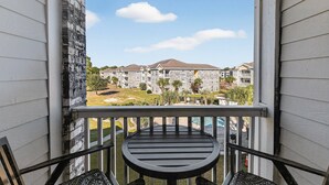 A balcony with a view of a residential complex, featuring a stone building and a grassy area.