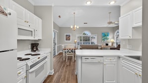 A kitchen with white cabinetry, a central island, and a dining area with a table and chairs. - Magnolia Place 4709-301 | Coastal feel | peaceful spot | walk to golf (Myrtle Beach)