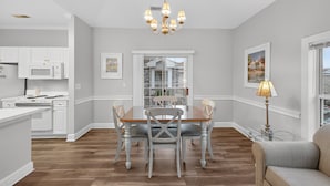 A modern kitchen with white cabinetry, a dining table with chairs, and a chandelier. - Magnolia Place 4709-301 | Coastal feel | peaceful spot | walk to golf (Myrtle Beach)