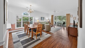 A spacious living room with a dining area, large windows, and a ceiling fan.