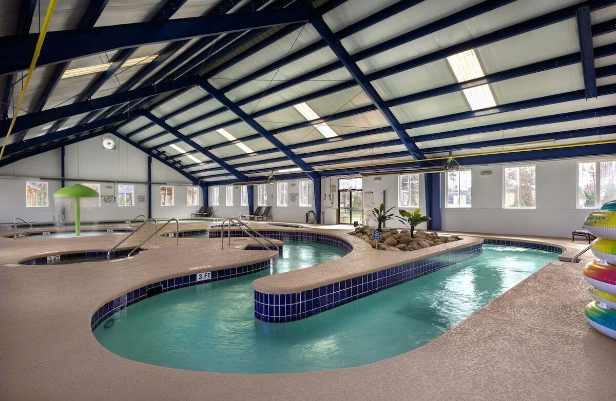 Une piscine intérieure dotée de plusieurs couloirs, d’un toit abrité et d’un espace détente avec des chaises.