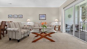 A living room with a glass coffee table, striped armchairs, a sofa, and a dining area with chairs and a table.