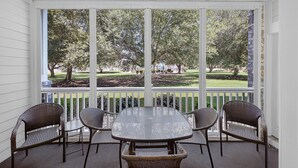 A covered patio with a table and four wicker chairs, overlooking a well-maintained lawn and trees.
