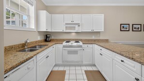 A kitchen with white cabinets, a granite countertop, a stove, and a microwave.