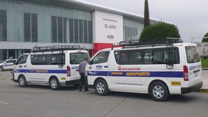 Twee witte bestelwagens met blauwe en gele markeringen staan voor een gebouw met grote ramen en een bord waarop 