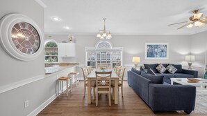 A modern living room with a dining area, featuring a large clock, a blue sofa, and a chandelier. - Magnolia Place 4661-101 | Myrtlewood Hit Greens, Then Hit the Couch (Myrtle Beach)