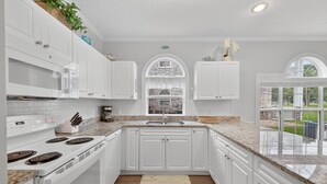 A modern kitchen with white cabinetry, granite countertops, and a large window offering a view of the outdoors. - Magnolia Place 4661-101 | Myrtlewood Hit Greens, Then Hit the Couch (Myrtle Beach)