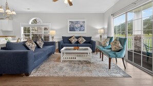 A spacious living room with a ceiling fan, two sofas, a coffee table, and a view of a garden through large windows. - Magnolia Place 4661-101 | Myrtlewood Hit Greens, Then Hit the Couch (Myrtle Beach)