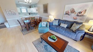 A modern living room with a grey sofa, a wooden coffee table, and a dining area with a kitchen in the background. - Myrtle Beach Golf Villa | Pool View | Blocks to Beach | Magnolia Place 4679-303 (Myrtle Beach)