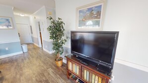 A living room with a flat-screen TV on a wooden stand, a potted plant, and a framed picture on the wall.
