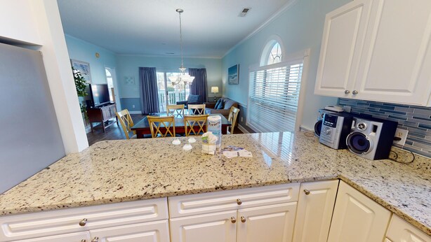 A kitchen with granite countertops, white cabinets, a dining area with a table and chairs, and a laundry area with a washing machine.