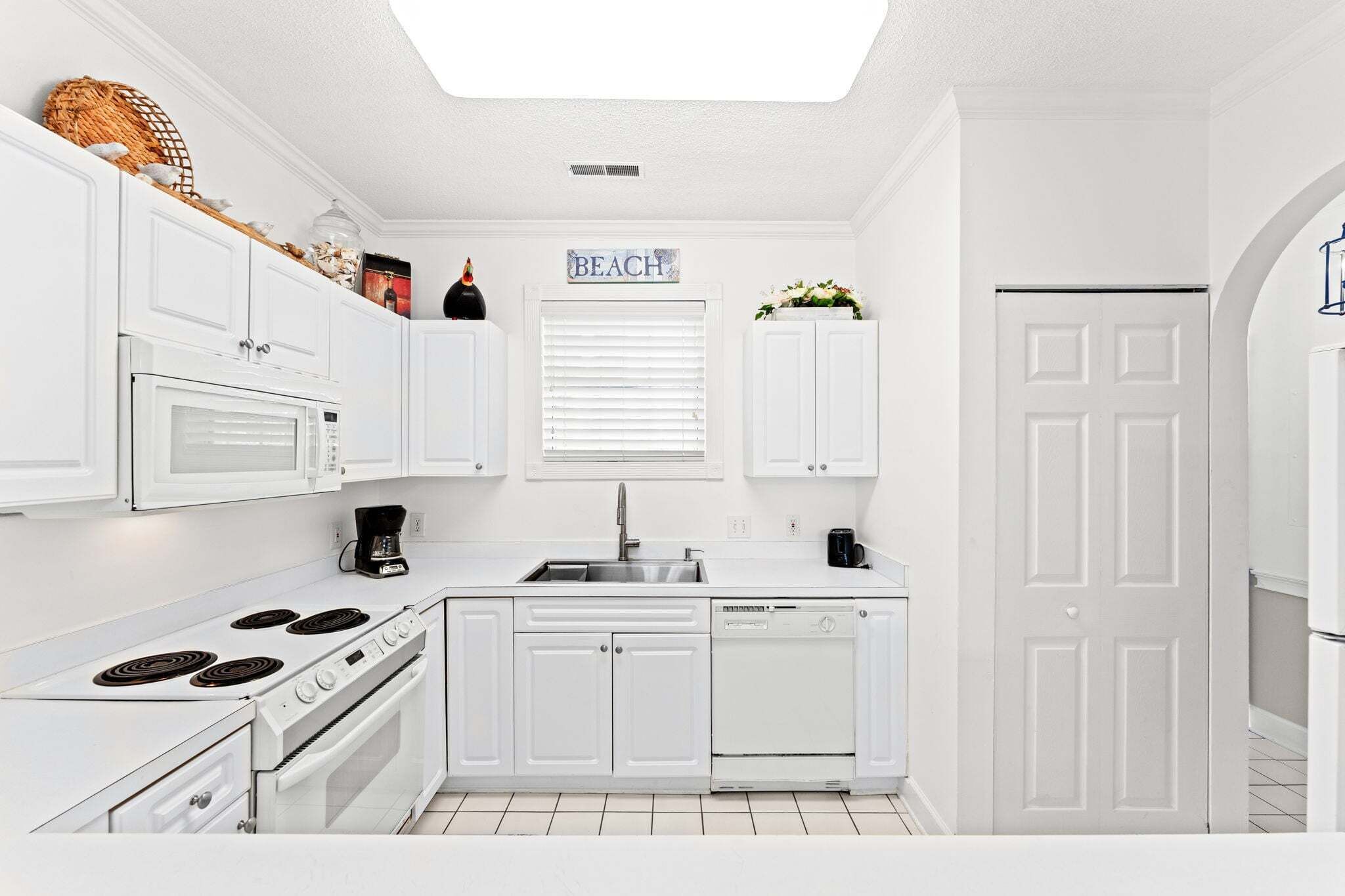 A white kitchen with a stove, microwave, sink, and dishwasher.