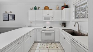 A modern kitchen with white cabinetry, a built-in microwave, a stove, and a sink. - Morning sun | golf fun | ocean breeze retreat | Magnolia Place 4701-103 (Myrtle Beach)