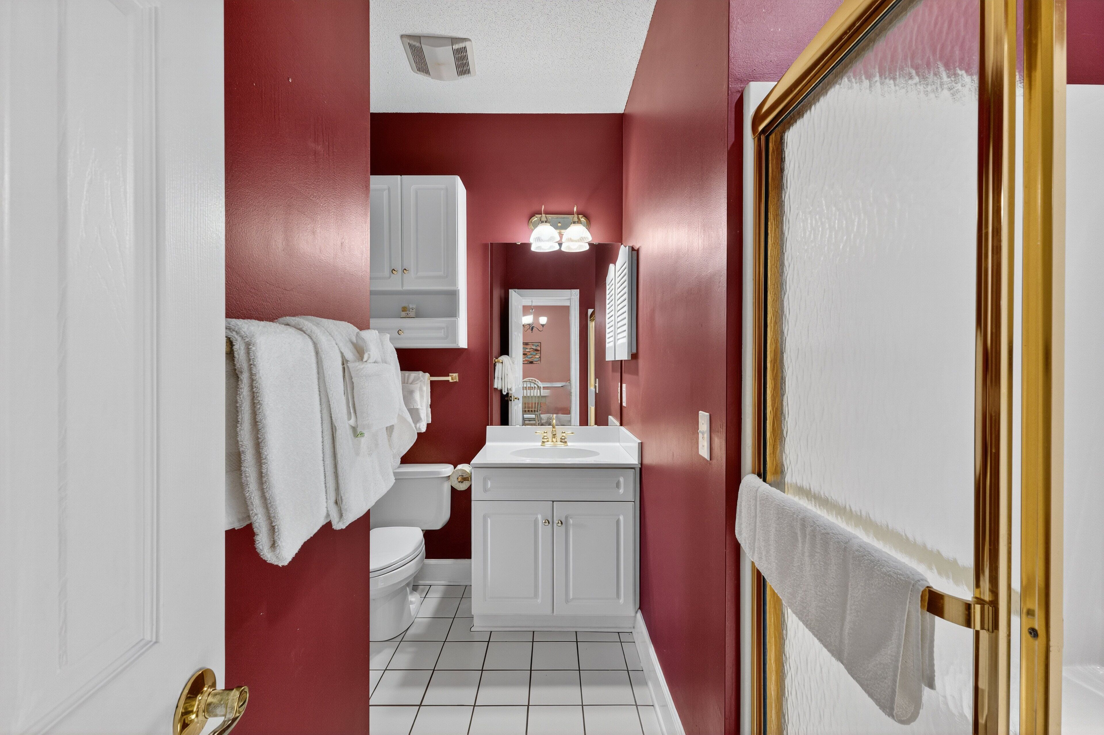 A bathroom with a red wall, white fixtures, and a gold-framed mirror.