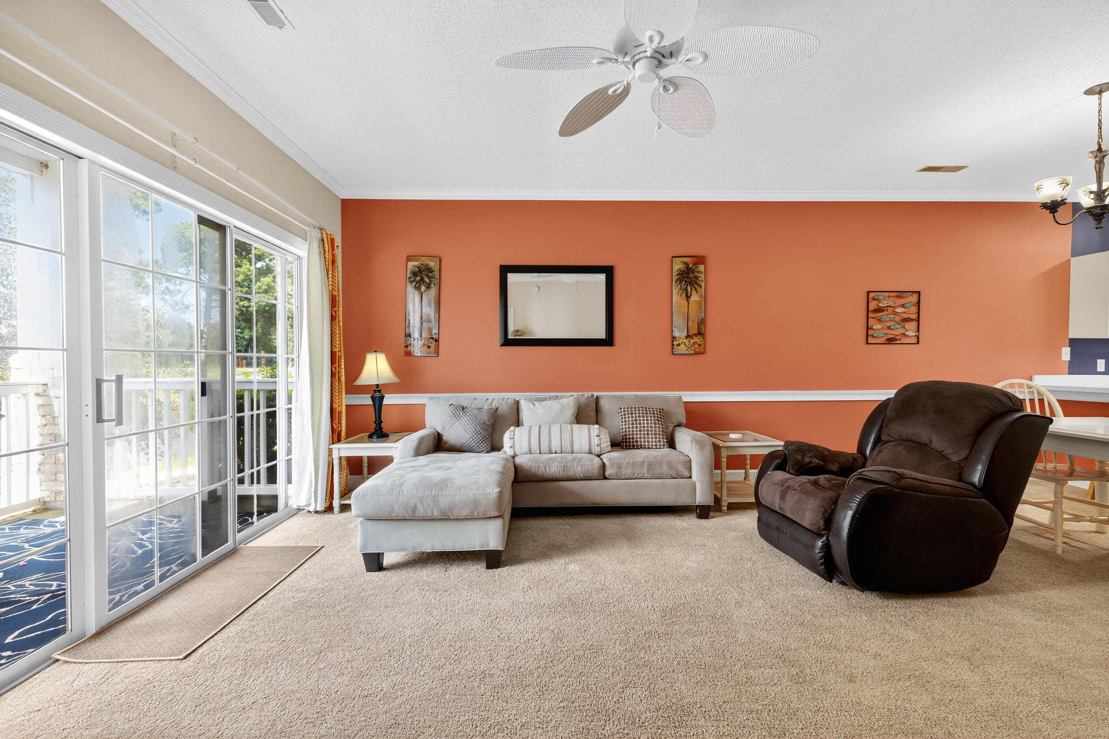 A living room with a sofa, ottoman, and recliner, a ceiling fan, and artwork on the walls.