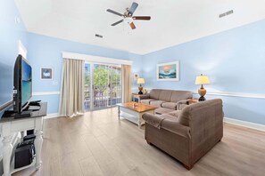 A living room with a sofa, coffee table, TV, and ceiling fan.